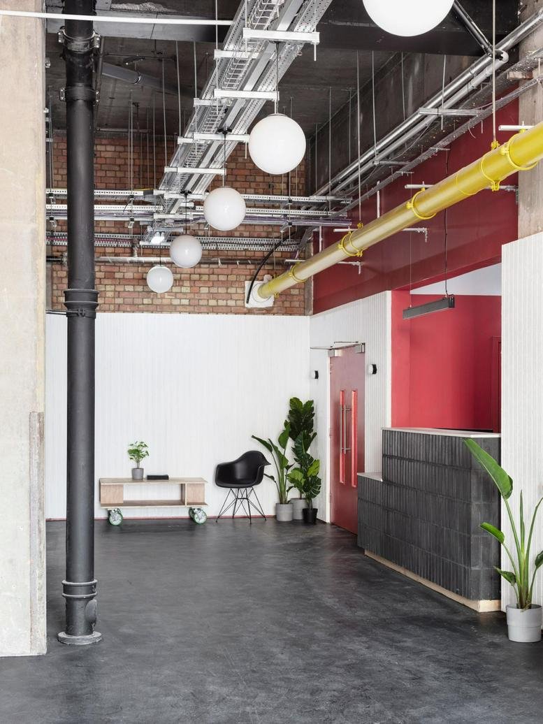 Vibrant reception lobby featuring exposed pipes, red walls, and a yellow air duct.