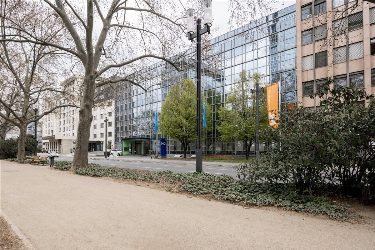 Modern glass exterior facade of Friedrich-Ebert-Anlage 36 near a tree-lined walkway.