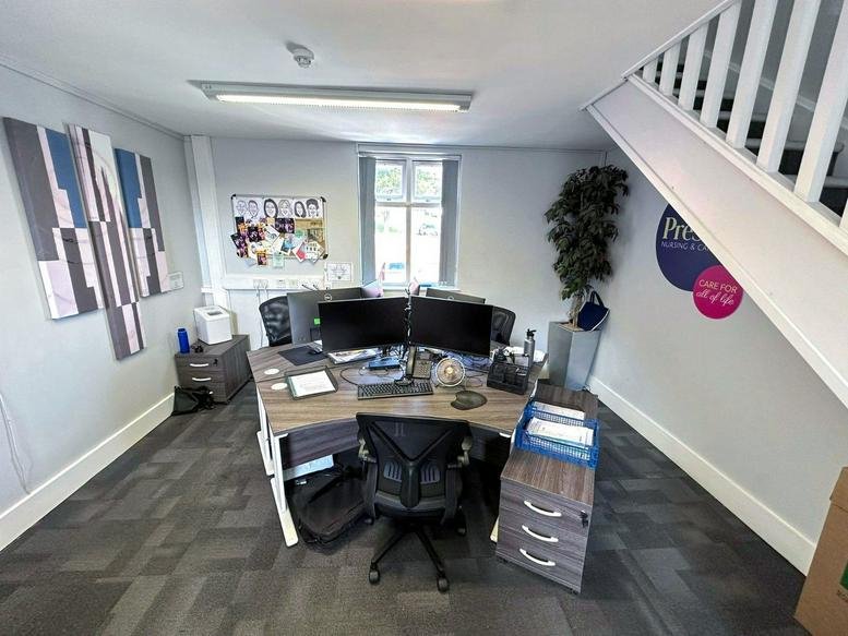 Open-plan workspace with a corner desk, office chair, and stairs in the corner.