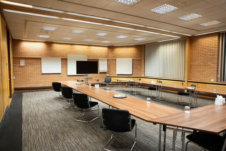 U-shaped boardroom with wooden tables, black chairs, and integrated AV equipment.