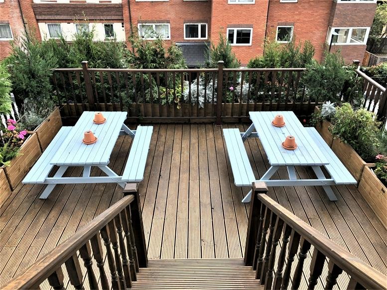 Outdoor wooden roof terrace at Highlands House with blue picnic tables and perimeter greenery.