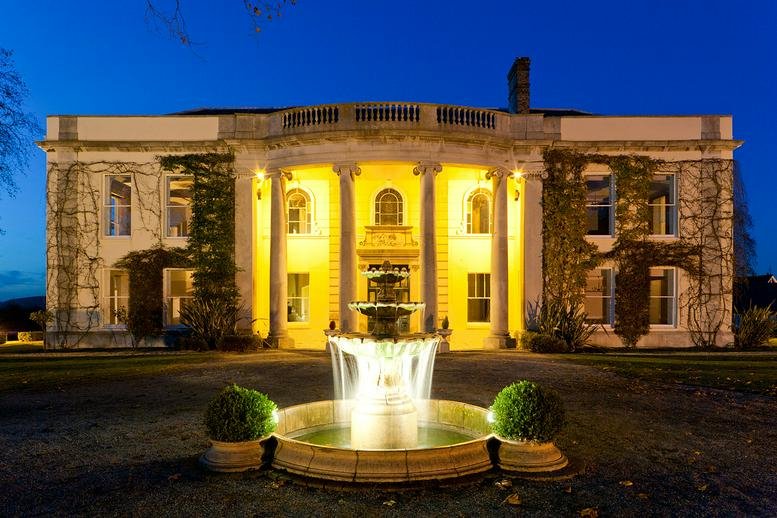 Exterior view of the grand white facade of the Business Centre, Horseshoe Hill at night with a lit fountain.