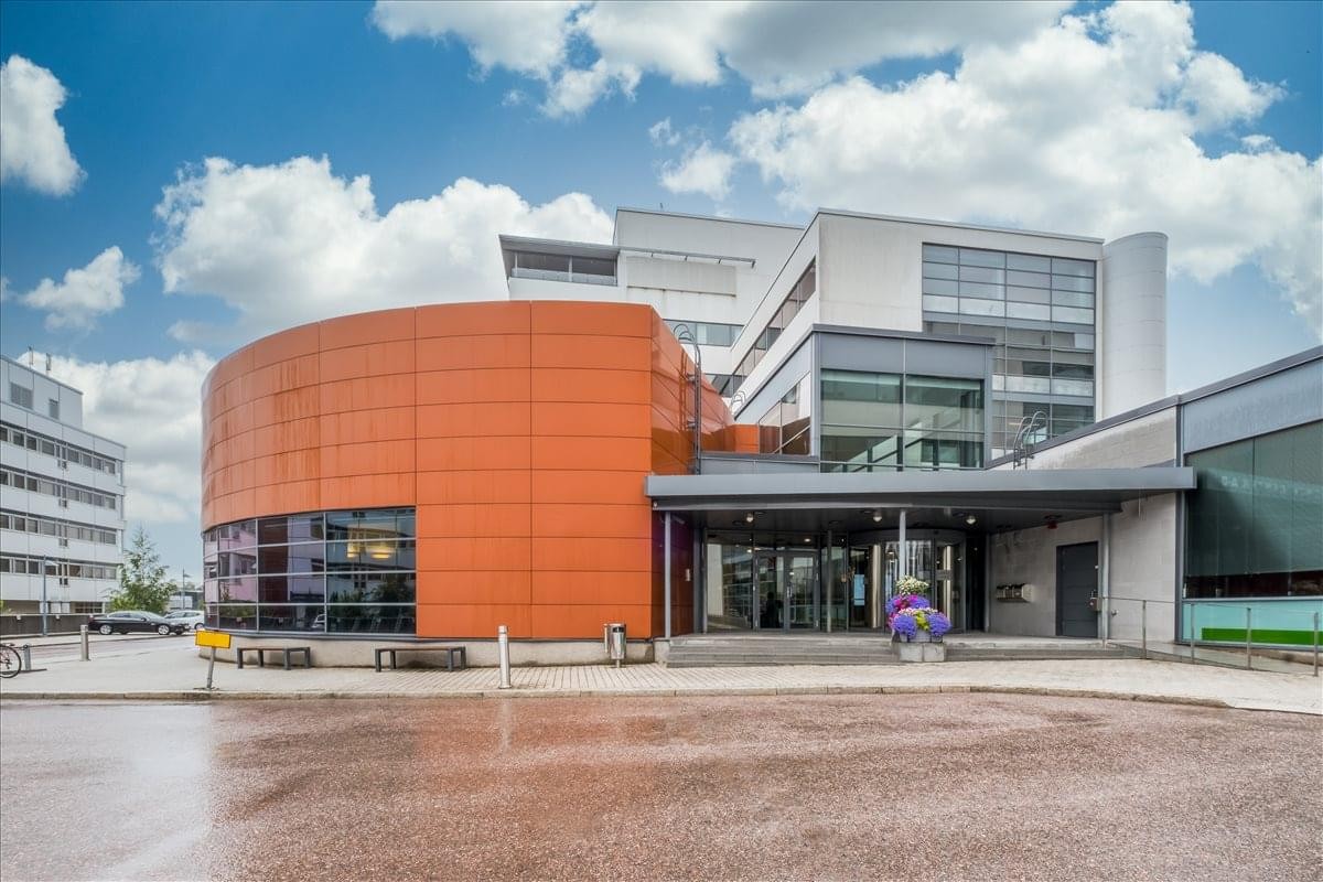 Exterior view of Keilaranta 16 featuring its distinct curved orange facade and glass entrance.