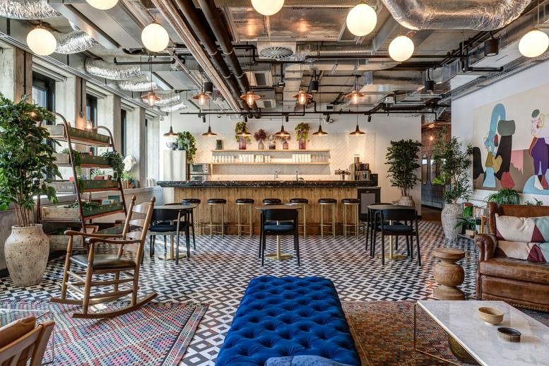 Spacious communal lounge at Koszykowa 61, Warsaw, Poland with eclectic seating, plants, and industrial ceiling.