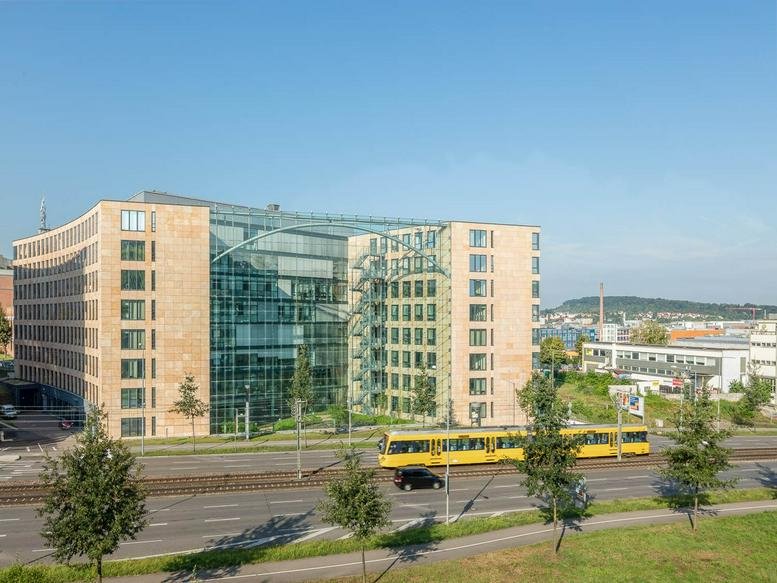 Wide view of the modern glass and sandstone facade with a yellow tram passing by.