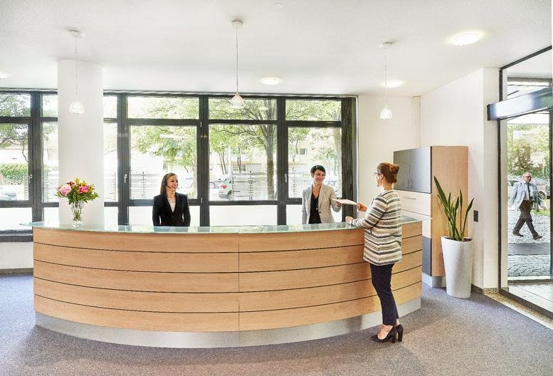Spacious wood-paneled reception area at Leopoldstrasse 244 with large windows and indoor plants.