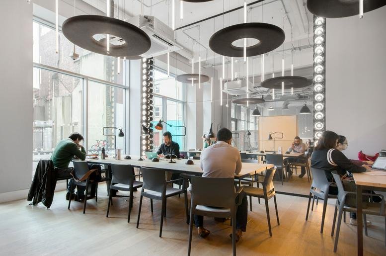 Lively co-working space with long communal tables and unique circular pendant lighting.