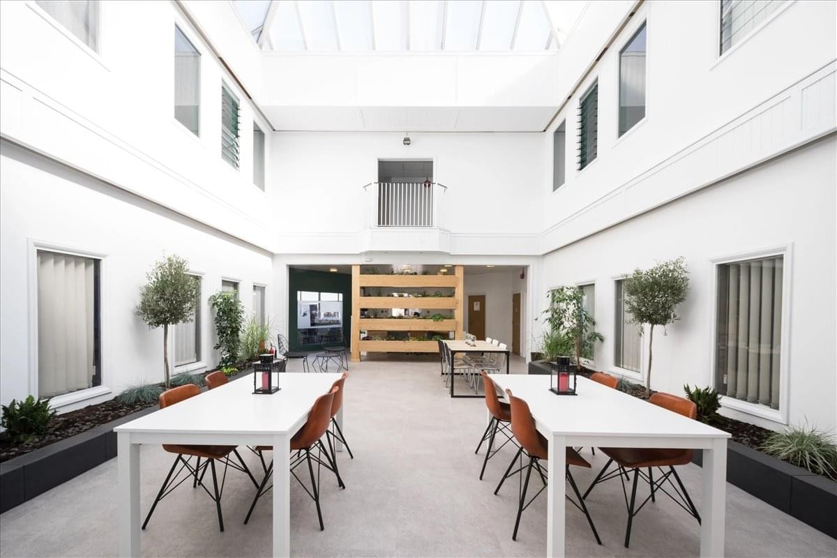 Spacious communal atrium at Lombard Business Park with white tables and skylights.