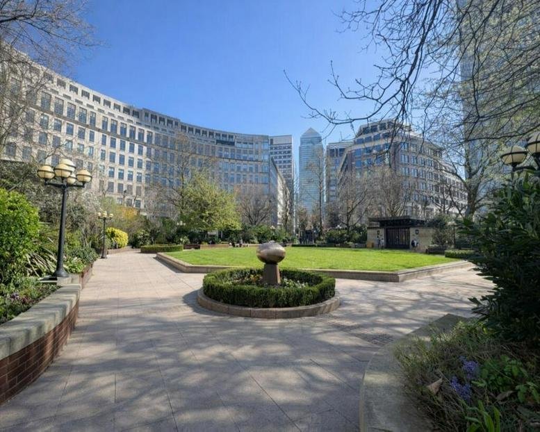 Public park with a fountain and green lawn surrounded by curved glass office buildings.