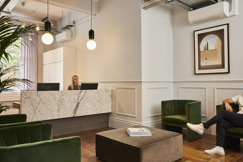 Reception desk with marble finish, green velvet armchairs, and warm pendant lighting.