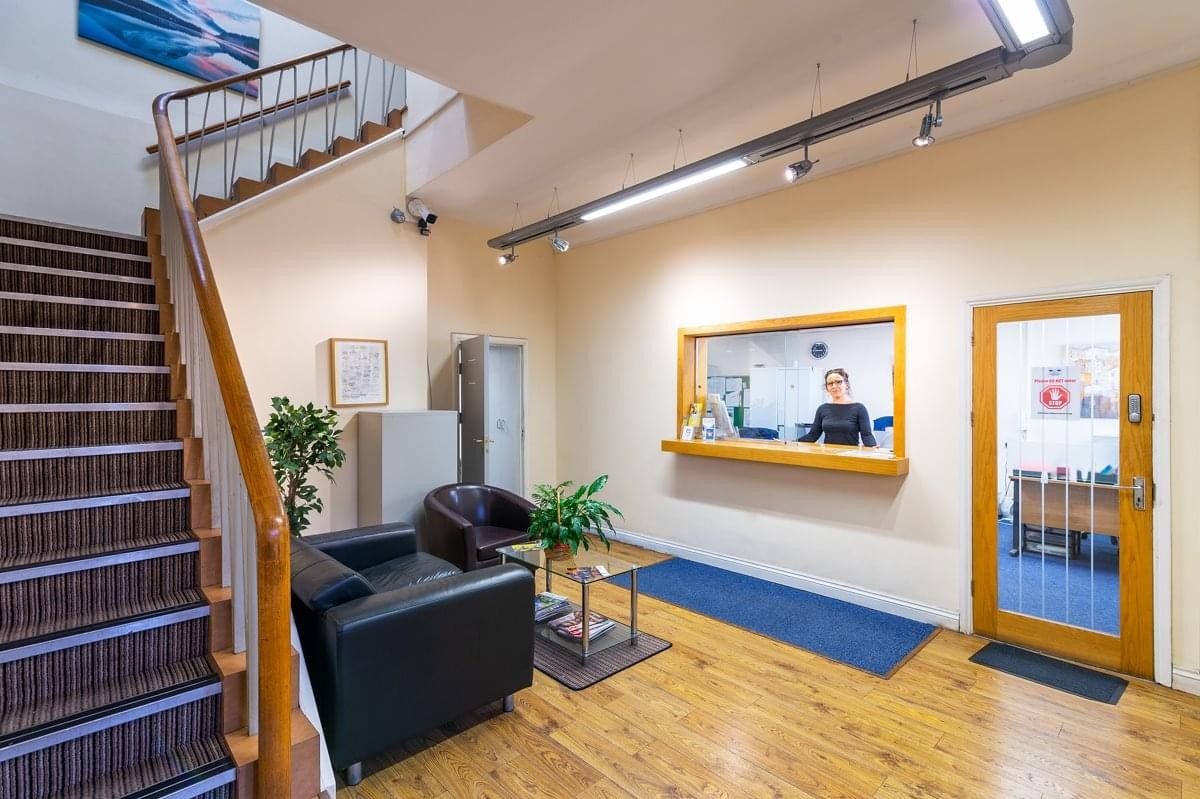 Bright reception area with wooden flooring, seating, and a staircase.
