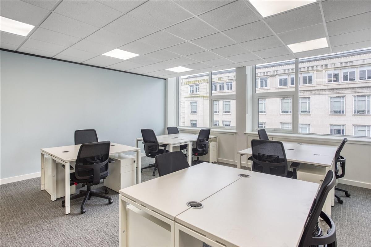 Spacious open-plan workspace at Merchants Court with white desks and large windows overlooking city buildings.