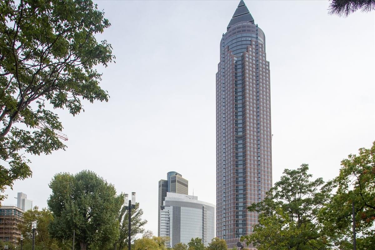 Exterior view of the iconic Art Deco style Messeturm Frankfurt skyscraper surrounded by trees.
