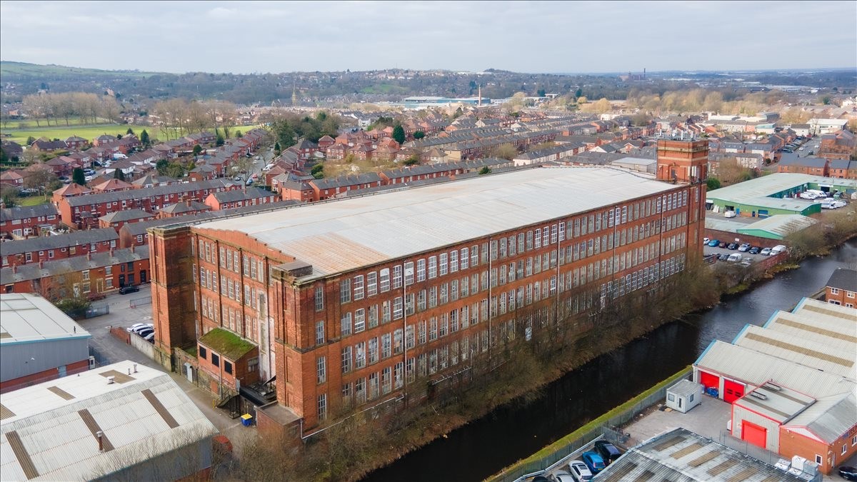Aerial exterior view of the historic red brick Moss Mill Industrial Estate beside a canal.