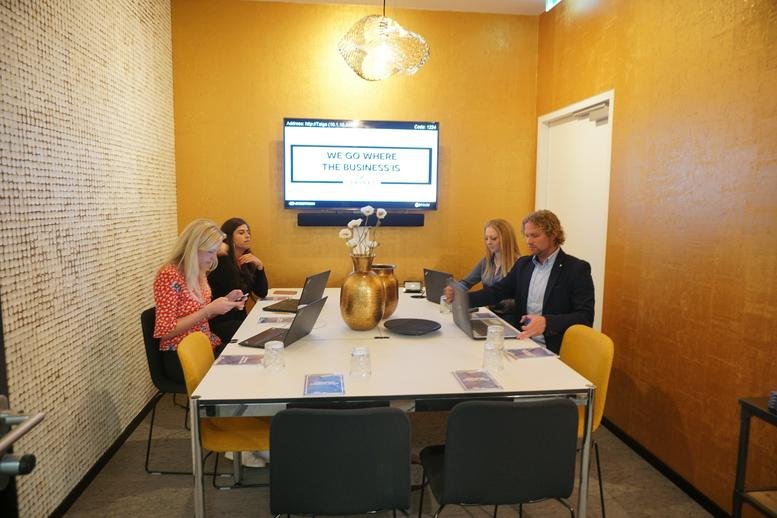 Team meeting in a modern conference room at Neue Mainzer Str. 46-50 with warm yellow walls and a wall-mounted screen.