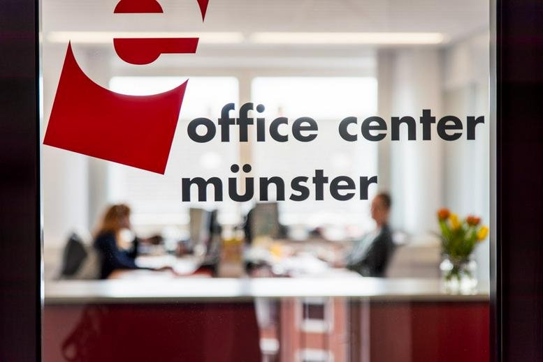 Glass entrance at Office Center Münster showing a reception desk and staff.