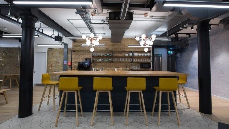 A stylish kitchen and breakout area at Notcutt House featuring a wooden bar and yellow high-top chairs.