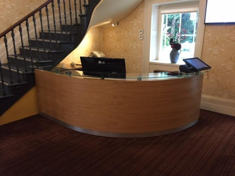Curved wooden reception desk with a computer monitor located near a classic staircase.