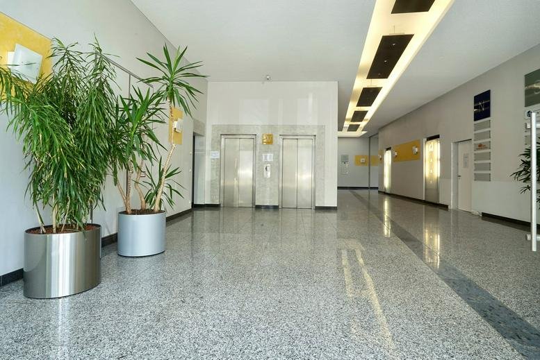 Spacious building lobby with polished granite floors, indoor plants, and elevator bank.