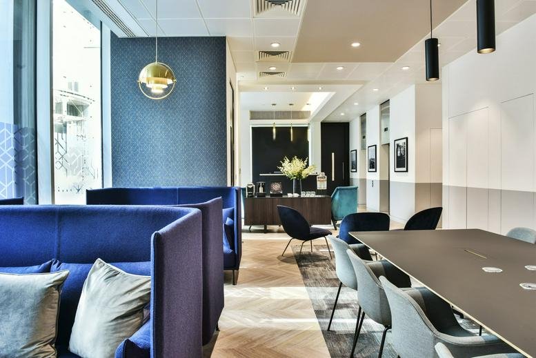 Bright coworking space with navy blue high-back sofas and wood-style flooring.