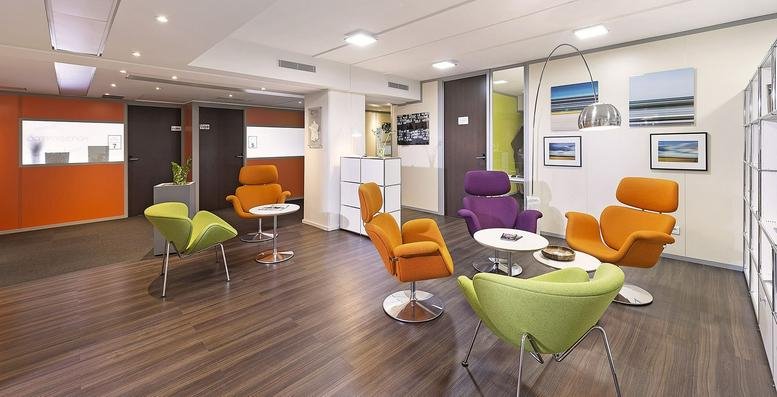 Spacious communal lounge at Parc d’activités La Ravoire with colorful chairs and modern wood flooring.