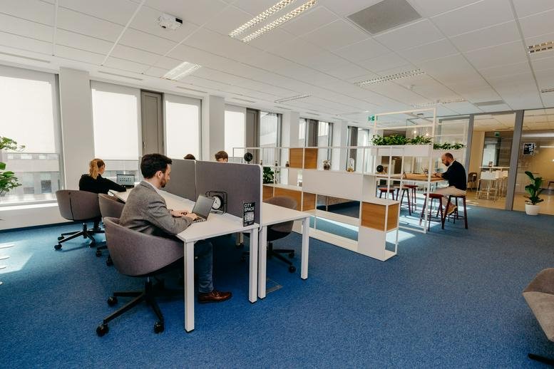 Open-plan workspace with white desks, grey dividers, and large windows.