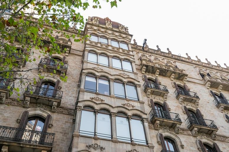 Exterior view of the ornate stone facade and balconies at Paseo de Gracia 12, 1ª Planta, Barcelona, Spain.
