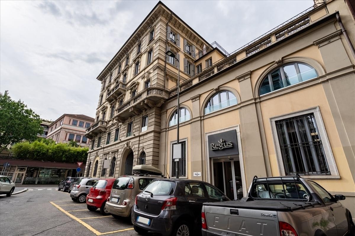 Classic exterior stone facade of the Piazzale Biancamano 8 building with parked cars in front.