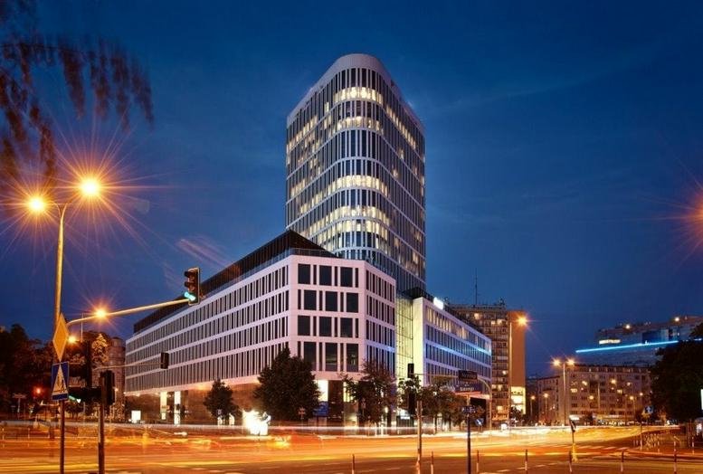 Exterior view of the illuminated glass facade of Plac Unii, Puławska 2 Street, Building B, Warsaw at dusk.