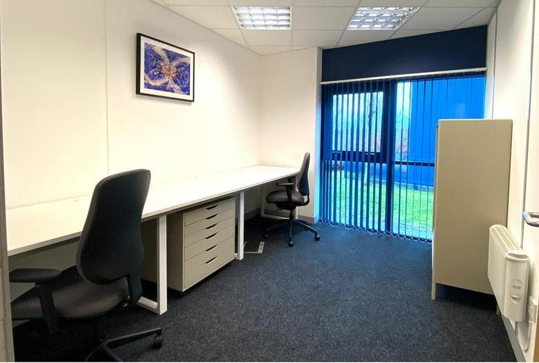 Bright private office suite featuring a long white desk and blue vertical blinds.