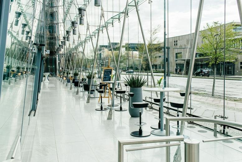 Bright glass-walled lobby with high ceilings and small café tables.