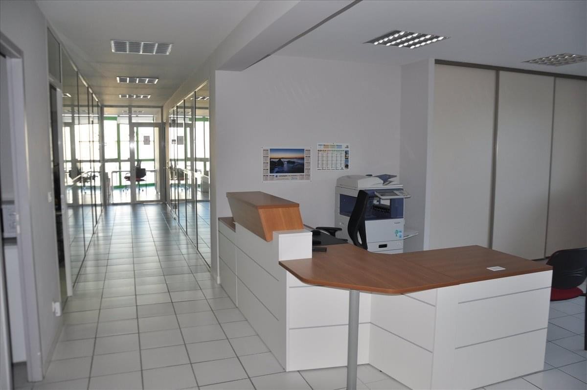 Modern reception area with a white and wood desk and a long tile-floor corridor.