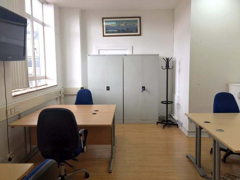 Spacious interior office space at Putney Studios featuring multiple desks, blue chairs, and natural window light.