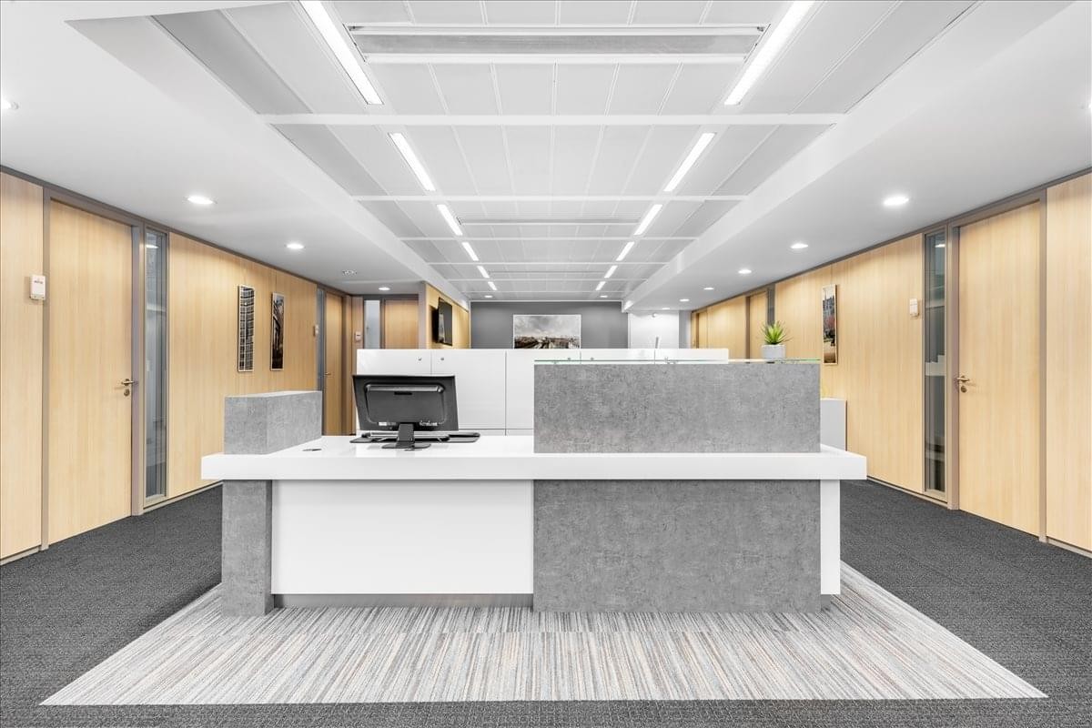 Modern reception area at Rond-Point Schuman 11 with a grey stone desk and light wood walls.