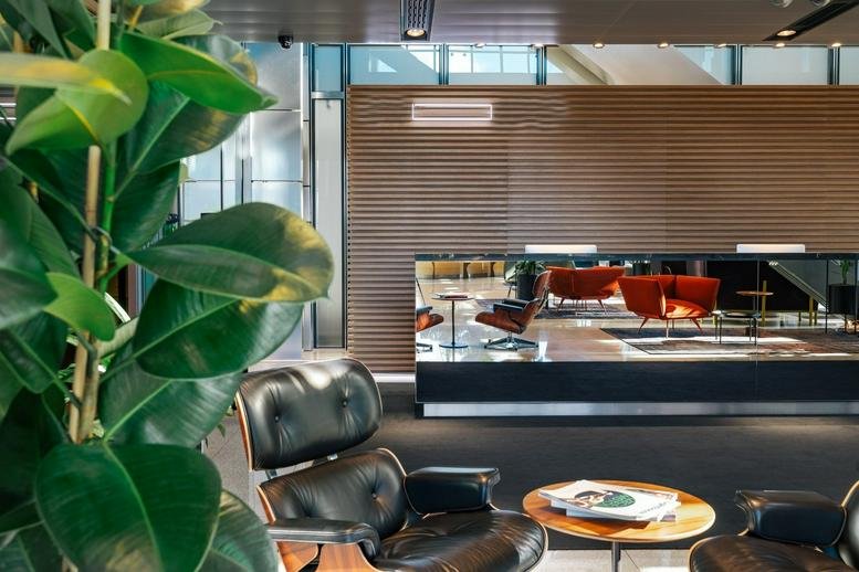 Modern lobby at Rondo ONZ 1 with stylish wood paneling, designer leather chairs, and lush green plants.