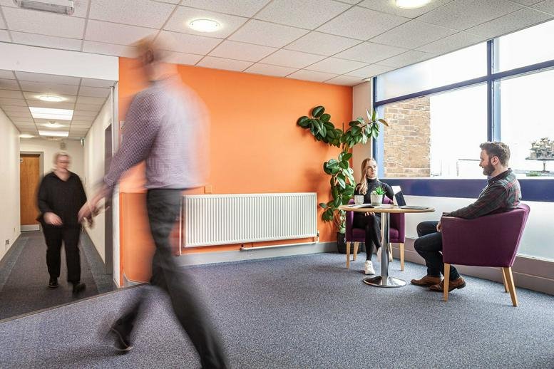 Spacious breakout area at Rosyth Business Centre, 16 Cromarty Campus with orange feature wall and lounge seating.