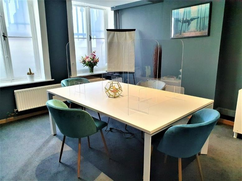 Modern meeting room with a white table, teal velvet chairs, and a glass partition.