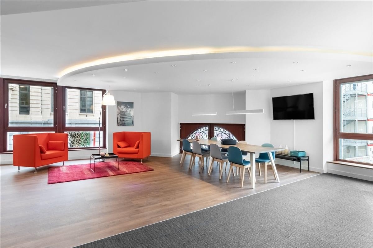 Modern lounge area with vibrant red armchairs, a long meeting table, and a wall-mounted TV.