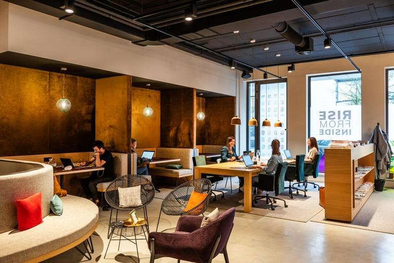 Warm coworking lounge featuring wood-paneled booths, designer chairs, and a long communal table.
