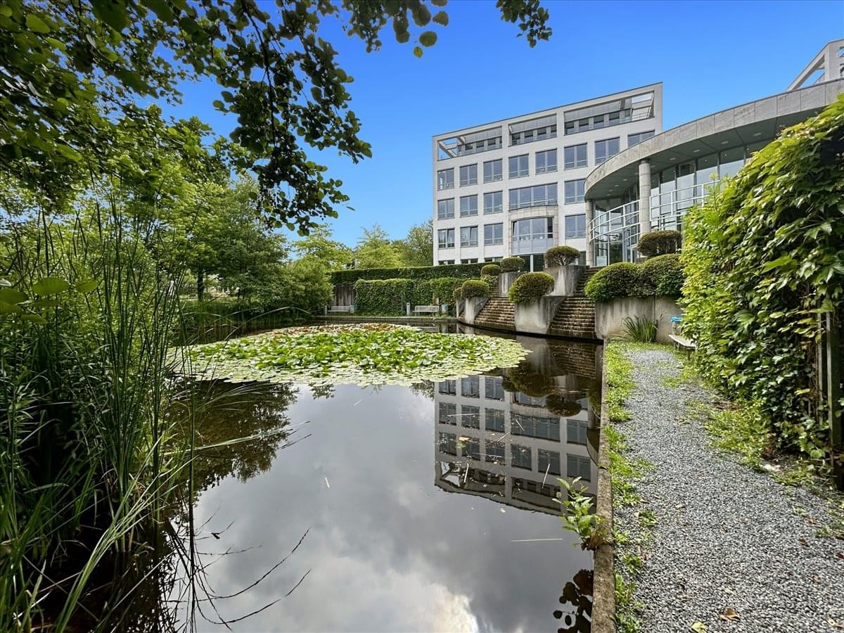 View of the modern glass-facade Ruhrallee 185 building reflected in a garden pond.