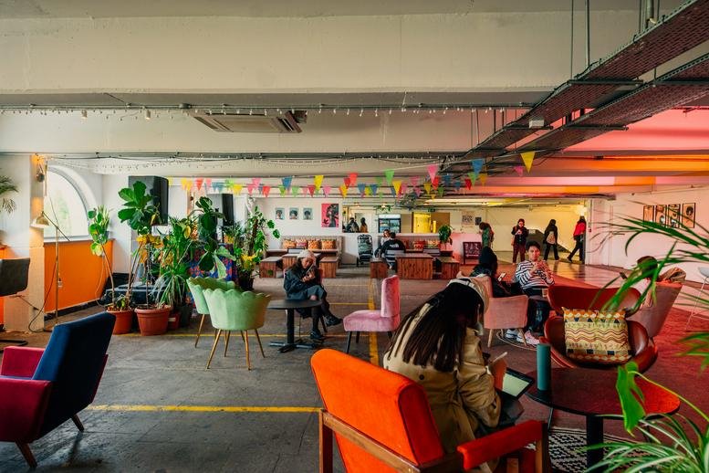 Large colorful communal lounge with eclectic furniture, potted plants, and festive bunting.