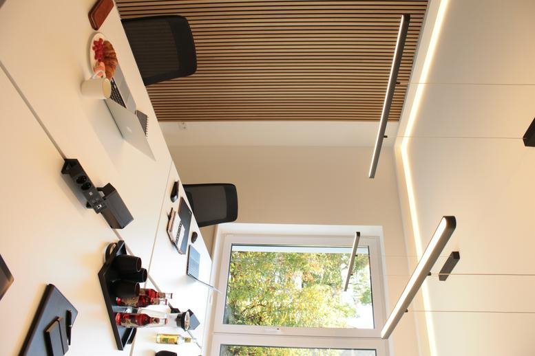 Close-up of a white office desk with power hubs and a view through a large window to green trees.
