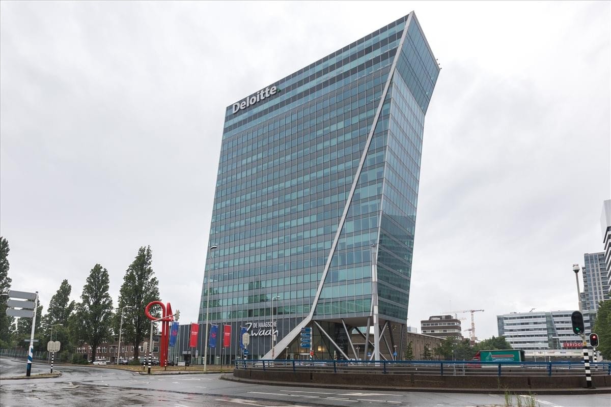 The striking angular glass exterior of De Haagsche Zwaan building under a cloudy sky.