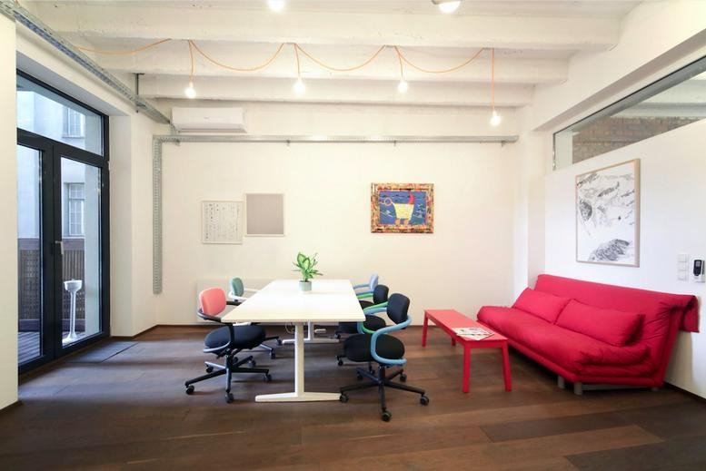 Spacious meeting room at Schottenfeldgasse 85 with a white table, red sofa, and artwork.