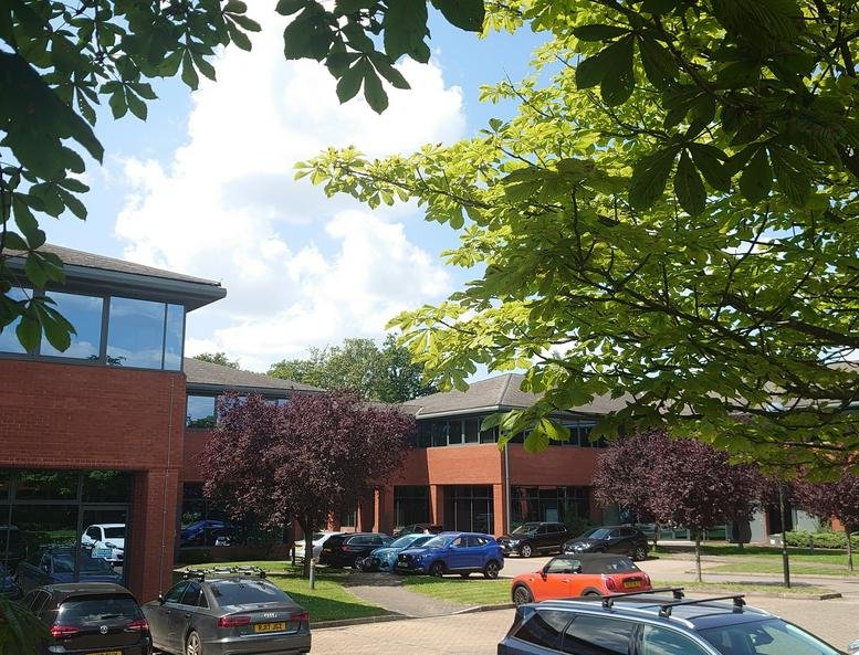 Exterior brick facade of Sentinel House at Ancells Business Park surrounded by lush green trees.