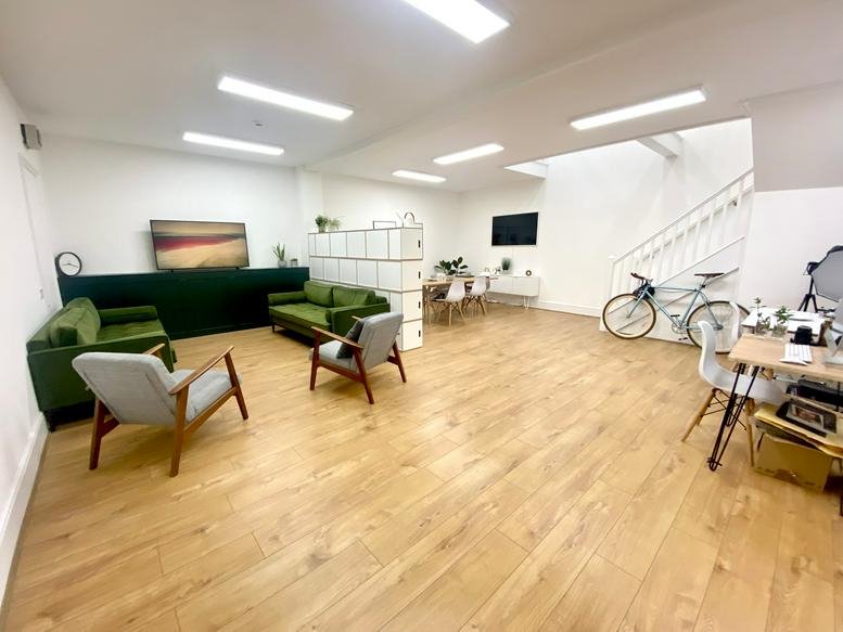 Bright communal lounge with green velvet sofas, wooden floors, and a white shelving divider.