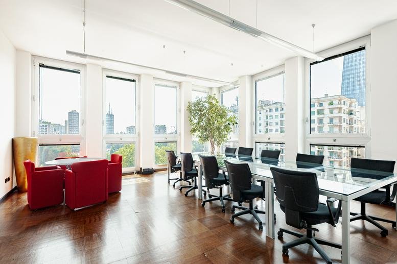 Spacious meeting room with red armchairs, large table, and city views through floor-to-ceiling windows.