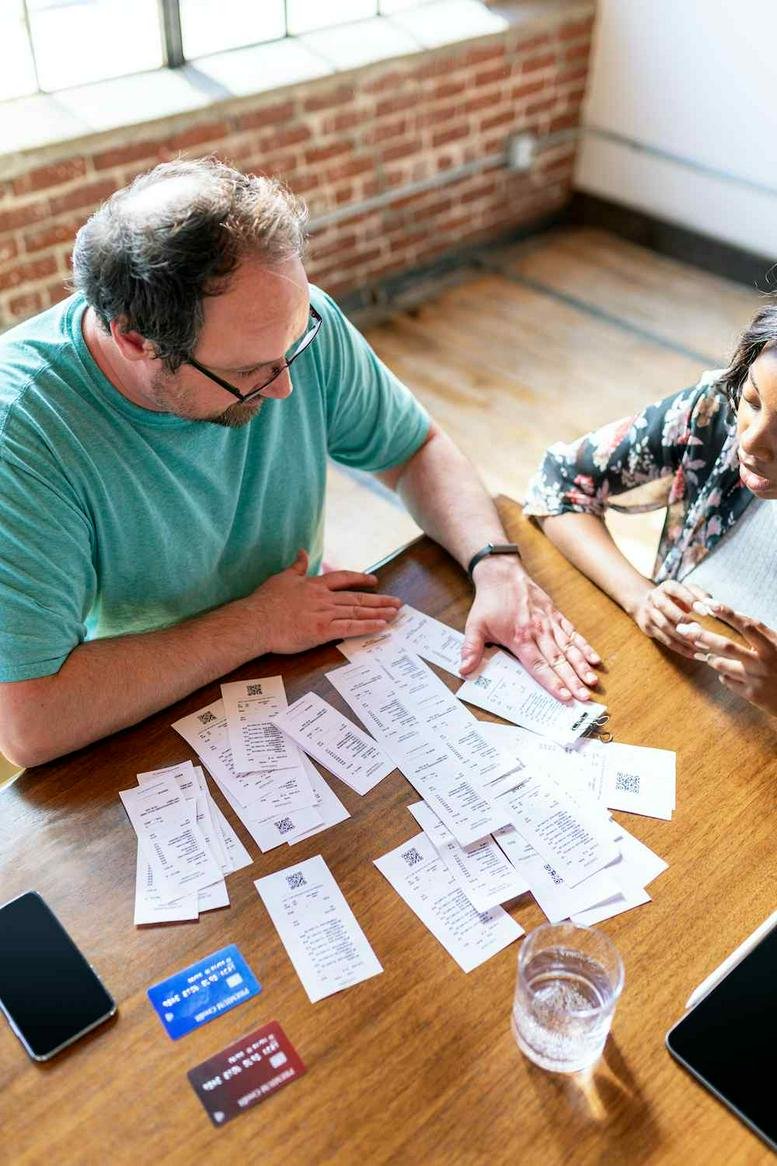 Man in a green shirt reviewing receipts on a wooden table.
