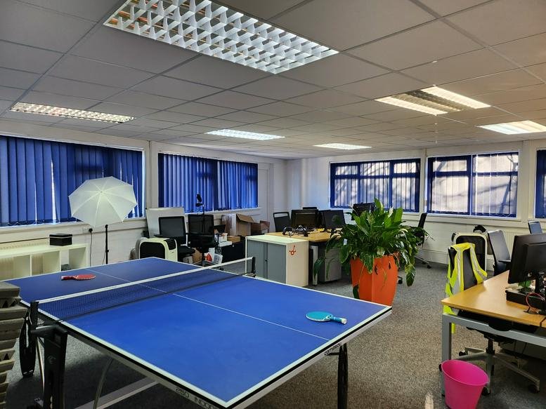 Spacious communal breakout area featuring a blue ping-pong table and potted plants.
