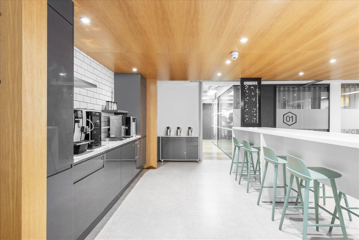 Modern communal kitchen and breakout area with wooden ceilings and mint green bar stools.
